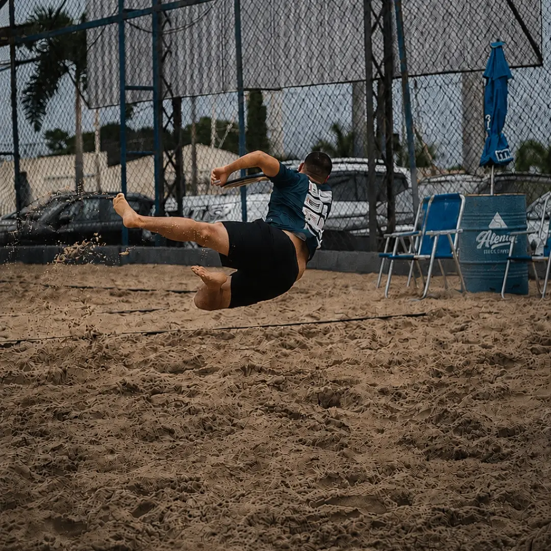 Atleta salta na areia para alcançar a bola